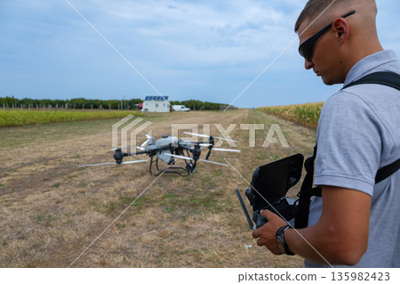 Drone pilot operating handheld controller in open field with quadcopter ready to fly 135982423
