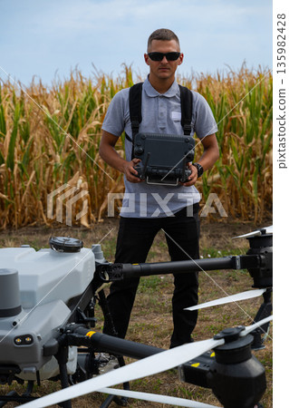 Drone pilot operating an agricultural drone in a cornfield with remote controller and safety gear Drone pilot operating an agricultural drone in a cornfield with remote controller and safety gear 135982428