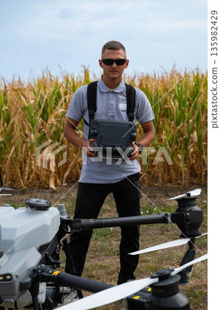 Drone pilot standing in a cornfield holding a controller for agricultural drone operations 135982429