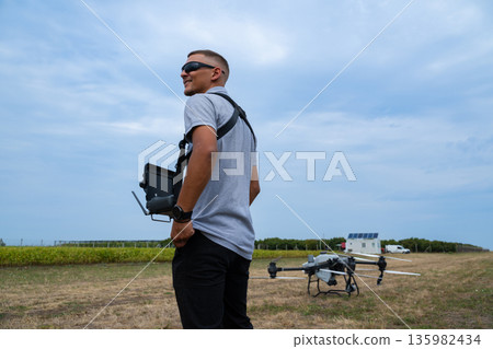 Drone pilot with controller stands in field preparing quadcopter for takeoff outdoors Drone pilot with controller stands in field preparing quadcopter for takeoff outdoors 135982434