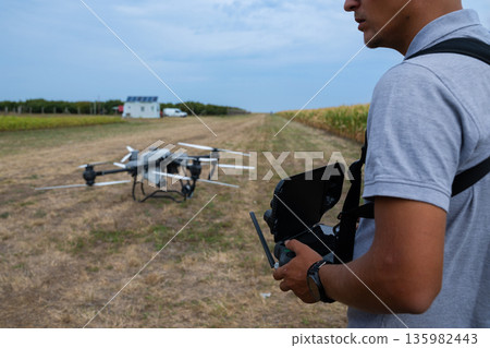 Drone pilot operates controller in a farmland field with a ground drone ready for flight 135982443