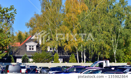 Cars parked at large parking lot. The back is a single family house covered with trees. 135982864