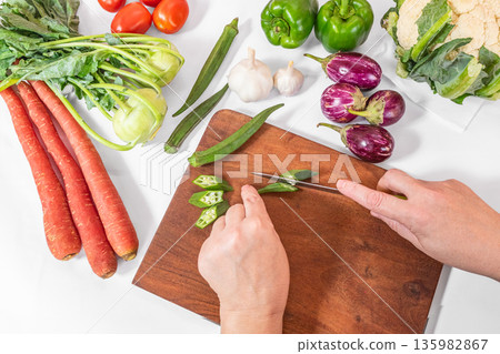 Woman hands cutting fresh vegetables on wooden cutting board, top view Woman hands cutting fresh vegetables on wooden cutting board, top view 135982867