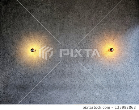 Two Modern Wall Sconces Illuminating a Textured Concrete Wall. Two Modern Wall Sconces Illuminating a Textured Concrete Wall. 135982868