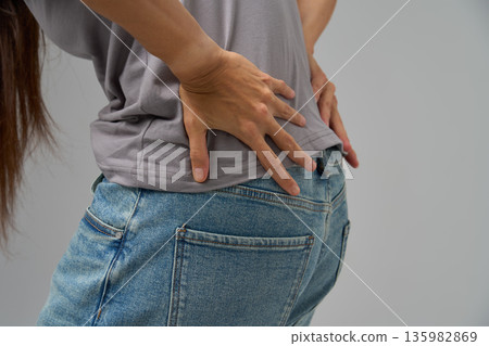 Close-up of person holding lower back in pain, showing discomfort  135982869