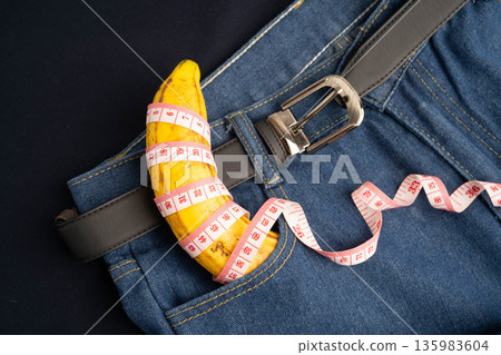 Banana with measuring tape on jean trousers, penis health. 135983604