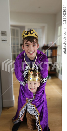 Two smiling children indoors wearing gold crowns and purple royal costumes 135983634