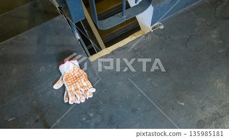 Construction gloves on an old stair landing in a multi-story building. Workwear and safety equipment for renovation or repair. Building maintenance. Construction gloves on an old stair landing in a multi-story building. Workwear and safety equipment for renovation or repair. Building maintenance. 135985181