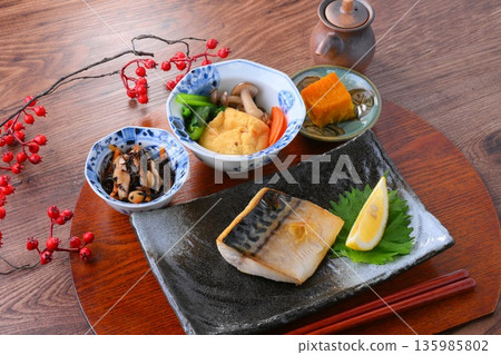 日式餐點，包括一份湯和三道小菜：米飯、味噌湯、一道小菜、一道小菜、烤鹹鯖魚、烤魚和梅子飯。 135985802