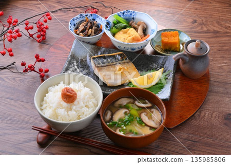 日式餐點，包括一份湯和三道小菜：米飯、味噌湯、一道小菜、一道小菜、烤鹹鯖魚、烤魚和梅子飯。 135985806