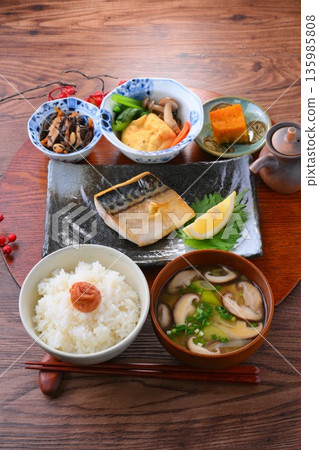 日式餐點,包括一份湯和三道小菜:米飯、味噌湯、一道小菜、一道小菜、烤鹹鯖魚、烤魚和梅子飯。 日式餐點,包括一份湯和三道小菜:米飯、味噌湯、一道小菜、一道小菜、烤鹹鯖魚、烤魚和梅子飯。 135985808