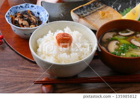 A Japanese meal consisting of one soup and three side dishes: rice, miso soup, a side dish, a side dish, grilled salted mackerel, grilled fish, and rice with pickled plums. 135985812
