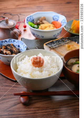 日式餐點,包括一份湯和三道小菜:米飯、味噌湯、一道小菜、一道小菜、烤鹹鯖魚、烤魚和梅子飯。 日式餐點,包括一份湯和三道小菜:米飯、味噌湯、一道小菜、一道小菜、烤鹹鯖魚、烤魚和梅子飯。 135985816