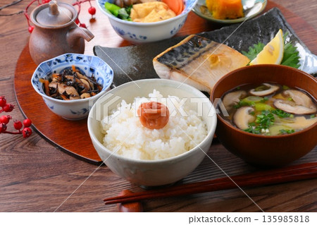 A Japanese meal consisting of one soup and three side dishes: rice, miso soup, a side dish, a side dish, grilled salted mackerel, grilled fish, and rice with pickled plums. 135985818