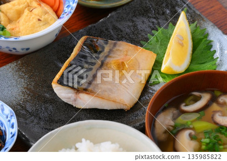 日式餐點,包括一份湯和三道小菜:米飯、味噌湯、一道小菜、一道小菜、烤鹹鯖魚、烤魚和梅子飯。 日式餐點,包括一份湯和三道小菜:米飯、味噌湯、一道小菜、一道小菜、烤鹹鯖魚、烤魚和梅子飯。 135985822