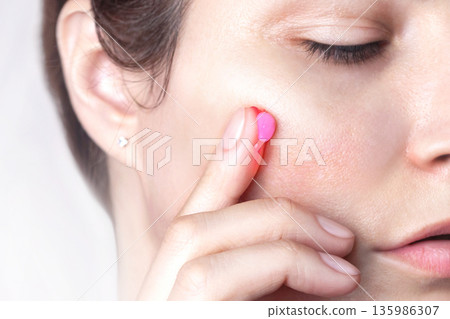 A drop of capsule pink cream on the finger of a woman. Caucasian woman applies cream to her face. Swatch of pink popular Niacinamide Capsule Cream. isolated on pink background photo 135986307