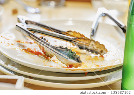 餐桌上擺放著飯後剩下的盤子和夾子。 餐桌上擺放著飯後剩下的盤子和夾子。 135987102