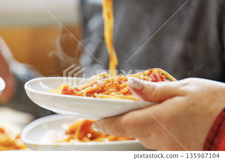 Steaming hot spaghetti in tomato sauce held high with tongs 135987104