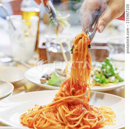 Steaming hot spaghetti in tomato sauce held high with tongs 135987108