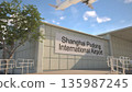 Shanghai Pudong International Airport entrance sign and airplane passing above on a summer day, Shanghai, China 3D rendering 135987245