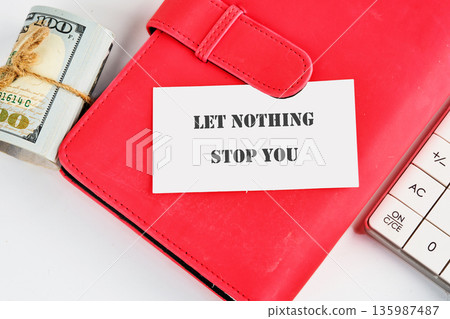 A red notebook holds a motivational card saying Let Nothing Stop You on a white table 135987487