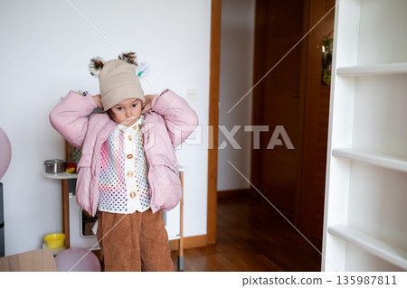 Young caucasian female child in winter coat and hat indoors 135987811