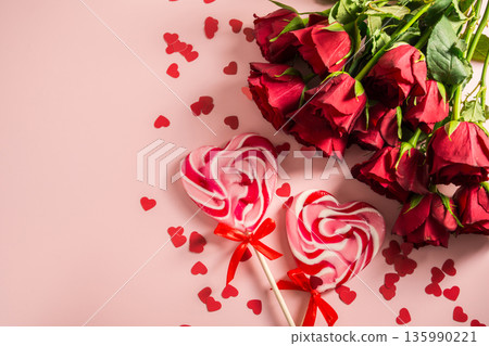 Valentine's Day background. Red roses and heart shaped lolly candy over pink background. Abstract flat lay. Celebrate, festive greeting card. Valentine's Day background. Red roses and heart shaped lolly candy over pink background. Abstract flat lay. Celebrate, festive greeting card. 135990221