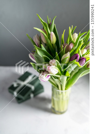 Spring floral background. Fresh purple and pink tulips flowers bouquet in glass vase and gift boxes. Mother's day. Copy space 135990241