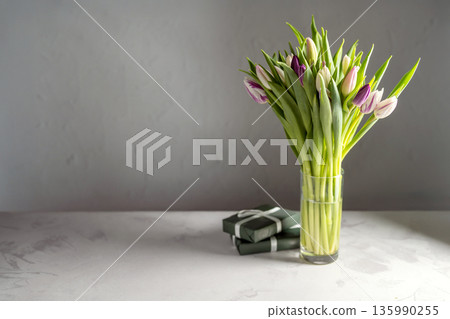 Spring floral background. Fresh purple and pink tulips flowers bouquet in glass vase and gift boxes. Mother's day. Copy space Spring floral background. Fresh purple and pink tulips flowers bouquet in glass vase and gift boxes. Mother's day. Copy space 135990255
