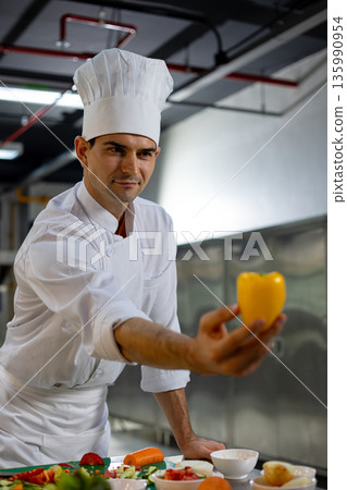Professional male chef in a clean commercial kitchen carefully selecting fresh yellow bell pepper, preparing healthy food with attention to quality, hygiene, and culinary craftsmanship 135990954