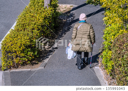 日本橫濱的城市景觀：光影交錯…老化社會：一位拄著拐杖的老婦人（戴著口罩）。她購物回家，左手戴著手套… 135991043