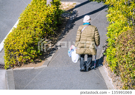 日本橫濱的城市景觀:光影交錯…老化社會:一位拄著拐杖的老婦人(戴著口罩)。她購物回家,左手戴著手套… 日本橫濱的城市景觀:光影交錯…老化社會:一位拄著拐杖的老婦人(戴著口罩)。她購物回家,左手戴著手套… 135991069