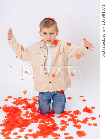 Little boy kneeling with falling red petals on white background. Valentines Day, joy, love, emotional and playful childhood scene 135991071