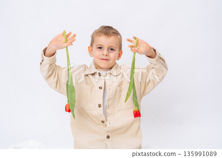 Happy little boy holding red tulips up on white background. Spring flowers, joy, childhood happiness 135991089