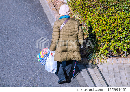 Yokohama cityscape in Japan: light and shadow... Aging society: An elderly woman with a cane (wearing a mask). On her way home from shopping, her left hand is gloved... 135991461