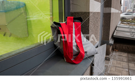 Forgotten textile shopper bag with purchases standing on a window ledge outside. Lost property at an urban building. Forgotten textile shopper bag with purchases standing on a window ledge outside. Lost property at an urban building. 135991661