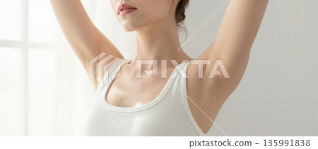 Minimal portrait of young woman stretching arms up in white tank top with soft natural light wellness concept 135991838
