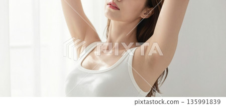Minimal portrait of young woman stretching arms up in white tank top with soft natural light wellness concept 135991839