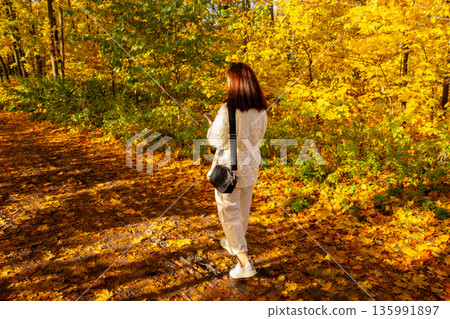 Woman using smartphone in autumn forest. Fall season stroll with digital device. Nature walk and technology balance. 135991897