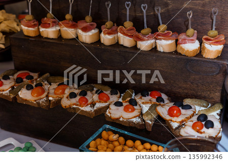 Assorted Spanish Tapas Displayed on Wooden Board with Olives, Ham, Cheese, and Pickles on Toasted Bread Slices Assorted Spanish Tapas Displayed on Wooden Board with Olives, Ham, Cheese, and Pickles on Toasted Bread Slices 135992346