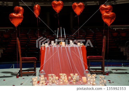 Romantic Valentine's Day Proposal Setup with Heart Balloons, Candlelit Table, and "MARRY ME" Lights in Theater Romantic Valentine's Day Proposal Setup with Heart Balloons, Candlelit Table, and "MARRY ME" Lights in Theater 135992353