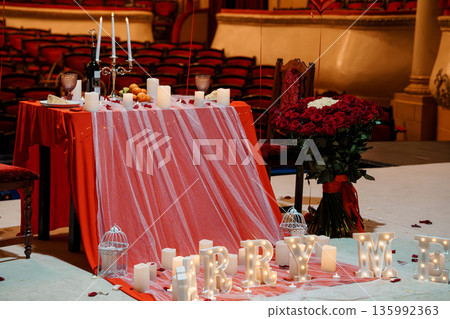 Romantic Proposal Setup in Grand Theater with Red Roses, Candlelit Table, and "MARRY ME" Lights Romantic Proposal Setup in Grand Theater with Red Roses, Candlelit Table, and "MARRY ME" Lights 135992363