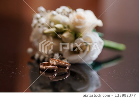 Elegant Rose Wedding Bouquet with Gold Rings on Reflective Surface in Soft Warm Lighting Elegant Rose Wedding Bouquet with Gold Rings on Reflective Surface in Soft Warm Lighting 135992377