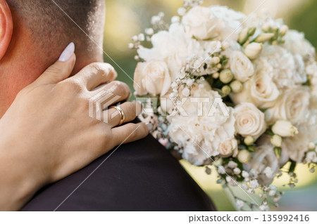 Romantic wedding moment with bride's hand gently resting on groom's shoulder holding white rose bouquet Romantic wedding moment with bride's hand gently resting on groom's shoulder holding white rose bouquet 135992416