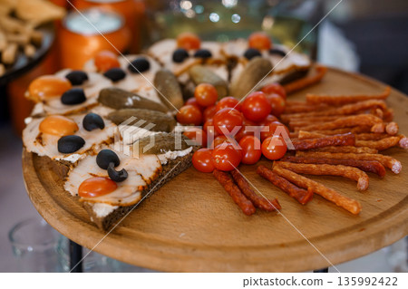 Assorted appetizer platter featuring smoked salmon toast, pickles, olives, cherry tomatoes, and sausages on a wooden serving board 135992422