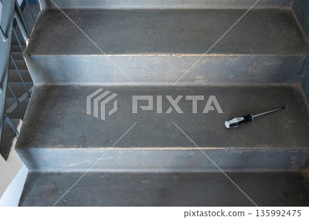 Screwdriver on gray concrete staircase. Maintenance and repair concept for construction, building, or renovation projects. Tool for home improvement. Screwdriver on gray concrete staircase. Maintenance and repair concept for construction, building, or renovation projects. Tool for home improvement. 135992475