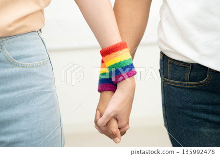 Asian LGBT couple woman holding hand wearing rainbow wristband. Asian LGBT couple woman holding hand wearing rainbow wristband. 135992478
