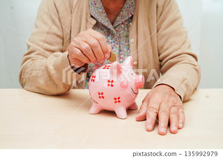 Retired elderly woman putting coins money in piggy bank and worry about monthly expenses and treatment fee payment. 135992979