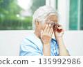 Asian senior woman wearing eyeglasses reduce headache and eyestrain suffer at home care service. 135992986