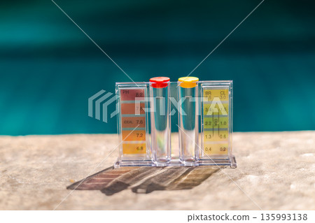 Pool water test kit with pH and chlorine scale on pool edge, maintenance concept with clear copy space and blue water background 135993138